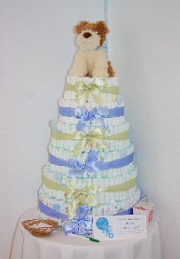 photo shows a large package cake of blue, gold and white. A puppy rest upon the top. What a great way to welcome in a new baby.