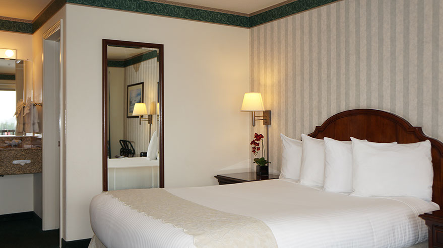 The Cozy Queen Guest Room Photo showing queen bed, night stand with lamp, full length mirror and entrance to wash/ dressing area.