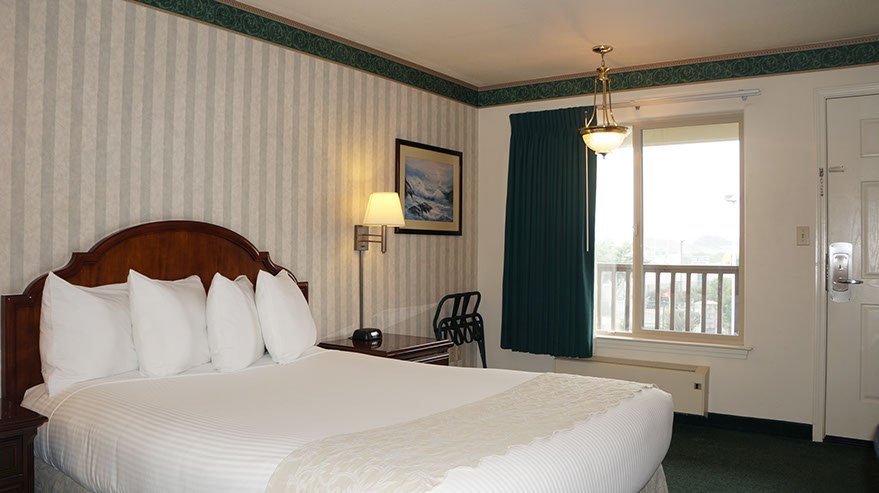 The Cozy Queen Guest Room Photo showing queen bed, night stand with lamp and alarm clock. Large viewing window and luggage rack.