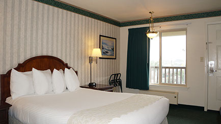 Photo showing queen bed, night stand with lamp and alarm clock. Large viewing window and luggage rack.