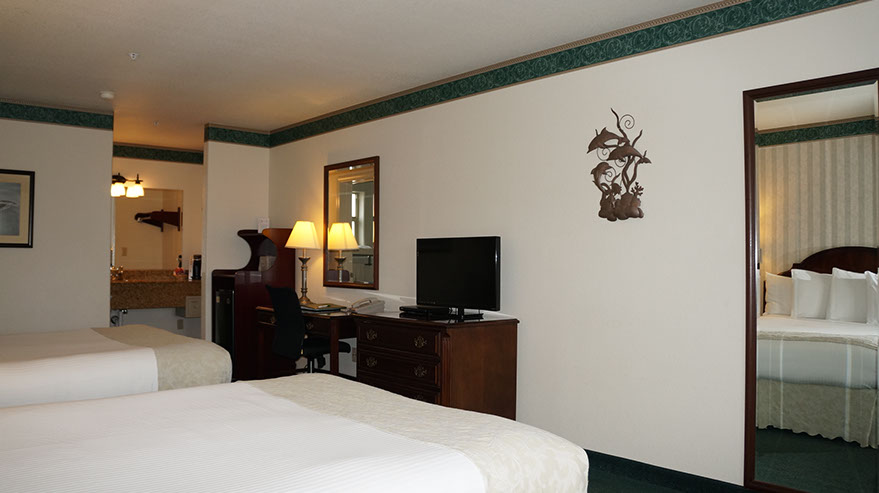 2 Queen Suite Guest Room photo showing 2 queen beds, dresser, flatscreen tv, writing desk, microwave, mini fridg and separate lighted dressing/wash area.