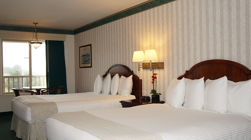 2 Queen Suite Guest Room Photo showing 2 queen beds, night stand with double lamps, table with 2 chairs next to a large viewing window.