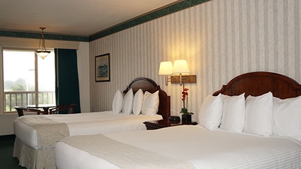 Photo showing 2 queen beds, night stand with double lamps, table with 2 chairs next to a large viewing window.