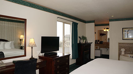 European King Size Bed guest room showing photo of partial bed, jacuzzi, chest of drawers with flat screen tv, writing desk, lamp, bathroom.