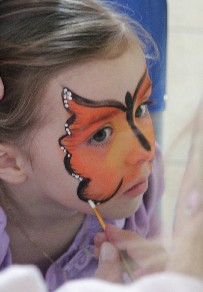 photo of a little girl getting a butterfly painted on her face.